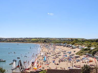 A beach with people swimming and sailing boats on the sand at 7 Maes Awel in Abersoch