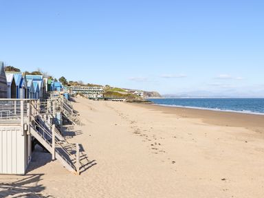 A sandy beach with wooden beach huts along the left side and the sea on the right at 7 Maes Awel in Abersoch