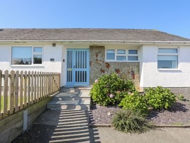 Front exterior of a single-story house with a light blue door and surrounding garden at 7 Maes Awel in Abersoch