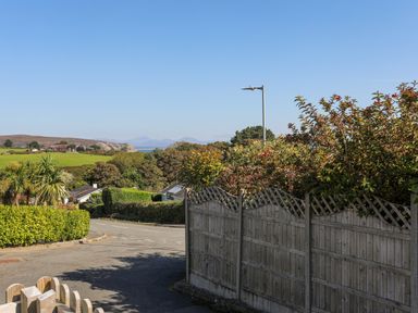 A road with wooden fences and bushes with hills and water in the background at 7 Maes Awel in Abersoch