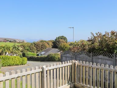 A wooden fence bordering a garden with trees houses and distant hills under a clear sky at 7 Maes Awel in Abersoch