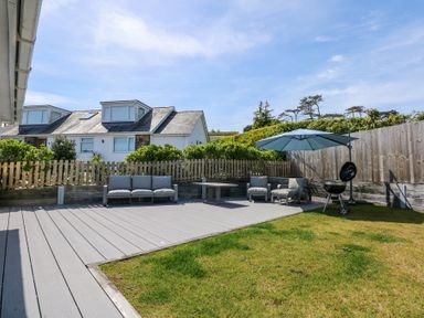 A backyard with a wooden deck seating area umbrella and barbecue at 7 Maes Awel in Abersoch