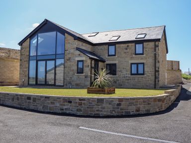 A stone house with large glass windows and a small lawn with a plant at The Waves in Amble