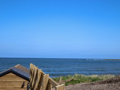A wooden fence and a small wooden building near the sea with grassy land at The Waves in Amble