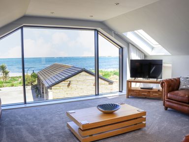 A living room with a large window overlooking the sea a wooden coffee table a television on a wooden stand and a leather sofa at The Waves in Amble