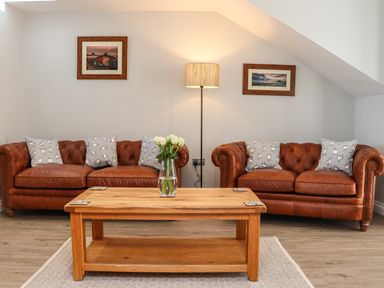 A living room with two brown leather sofas a wooden coffee table with a vase of flowers and a floor lamp at The Waves in Amble