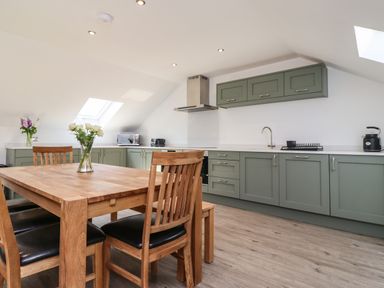 A kitchen with wooden dining table and chairs green cabinets and skylights at The Waves in Amble