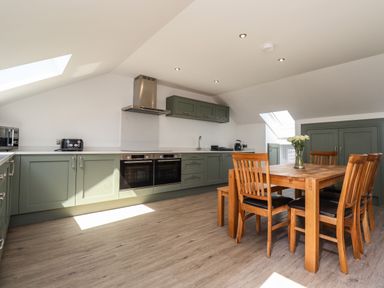 A kitchen with green cabinets wooden dining table and chairs and skylights at The Waves in Amble