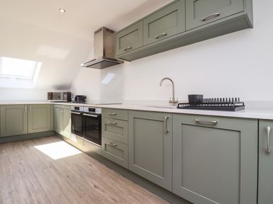 A kitchen with green cabinets a sink an oven microwave and dish rack at The Waves in Amble