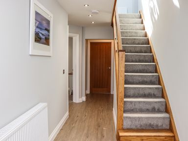 A hallway with wooden flooring a wooden staircase with carpet and a framed picture on the wall at The Waves in Amble