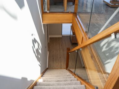 A staircase with carpeted steps and wooden glass railing leading to a wooden floor hallway with a small table at The Waves in Amble