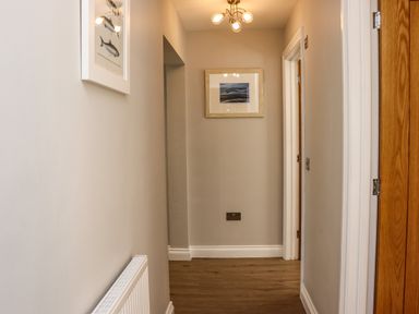 A hallway with wooden floor and beige walls with fish and landscape pictures at The Waves in Amble