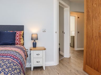 A bedroom with a bed beside a nightstand with a lamp and a wooden door open at The Waves in Amble