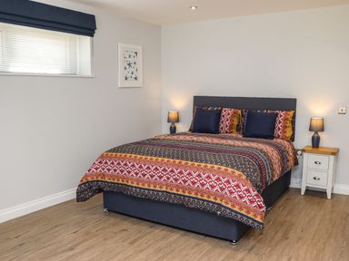 A bedroom with a patterned bedspread on a double bed bedside tables with lamps and a small window at The Waves in Amble