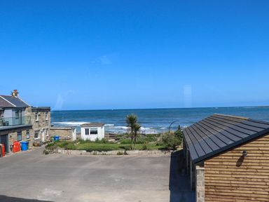 A view of the sea with buildings and a small garden area in front at The Waves in Amble