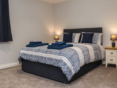 A bedroom with a bed covered in patterned bedding pillows and folded towels on top with two lit lamps on bedside tables at The Waves in Amble
