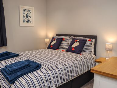 A bedroom with a double bed with striped bedding and puffin cushions at The Waves in Amble