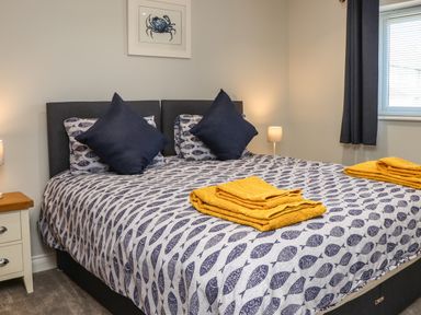 A bedroom with a bed covered in fish patterned bedding and yellow towels on the bed at The Waves in Amble