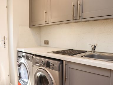 A laundry room with a washing machine dryer sink and gray cabinets at The Waves in Amble