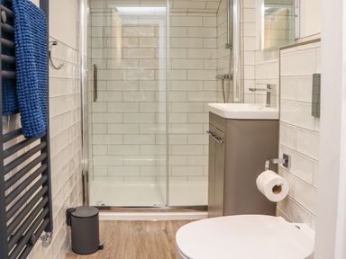 A bathroom with a shower enclosure sink toilet blue towels and a small trash bin at The Waves in Amble