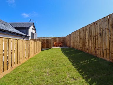 A grassy backyard area with wooden fences and a small table with chairs at The Waves in Amble