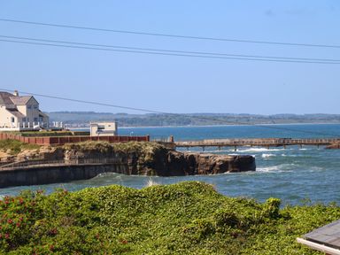 A coastal view with a house on a cliff and a wooden pier over the sea at The Waves in Amble