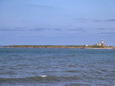 A coastal scene with a lighthouse and buildings on a flat island surrounded by water at The Waves in Amble