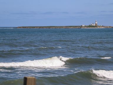 A view of the sea with waves and a small island with a lighthouse at The Waves in Amble