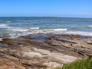 A coastal view with rocky shore and waves with a lighthouse on an island at The Waves in Amble