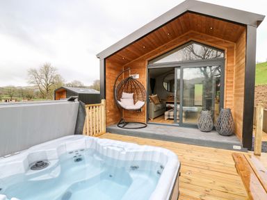 An outdoor deck with a hot tub a hanging chair and a wooden cabin with sliding glass doors at Fawn's Rest in Nantmel near Rhayader