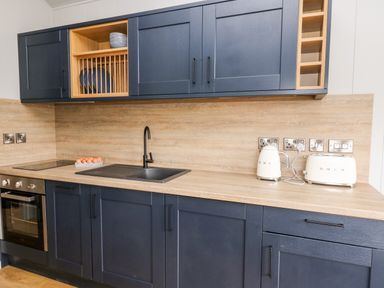 A kitchen with blue cabinets wooden countertops a black sink and faucet a toaster kettle and oven at Fawn's Rest in Nantmel near Rhayader