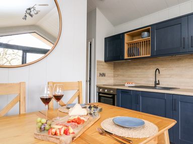 A kitchen with navy blue cabinets wooden countertop a sink and oven a dining table with two wine glasses a charcuterie board plates and chairs at Fawn's Rest in Nantmel near Rhayader