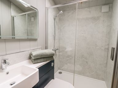 A bathroom with a sink, mirror, shower area with glass door, and folded towels on the counter at Fawn's Rest in Nantmel near Rhayader