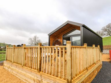A modern cabin with wooden deck and railing in a rural area at Fawn's Rest in Nantmel near Rhayader