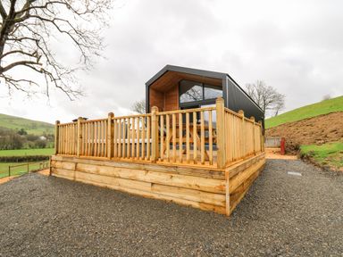 A modern cabin with wooden deck and railing in a rural grassy area at Doe Lodge Nantmel near Rhayader
