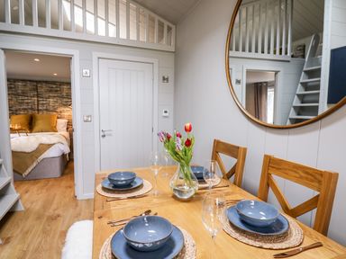 A dining area with a wooden table set with blue dishes and a vase of flowers next to a bedroom and staircase at Doe Lodge in Nantmel near Rhayader