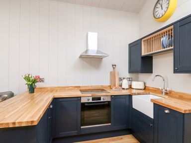 A kitchen with wooden countertops blue cabinets a white sink and a yellow wall clock at Doe Lodge in Nantmel near Rhayader