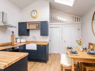 A kitchen and dining area with blue cabinets wooden countertops and a dining table set with blue bowls and glasses at Doe Lodge in Nantmel near Rhayader