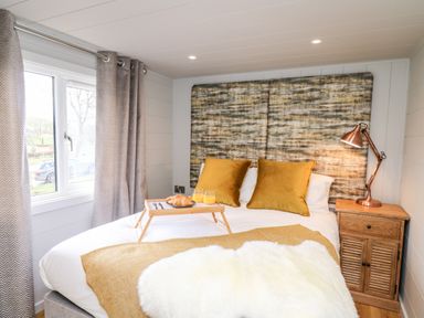 A bedroom with a bed with orange pillows and a breakfast tray next to a wooden nightstand with a lamp at Doe Lodge in Nantmel near Rhayader