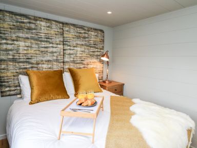 A bedroom with a bed with mustard pillows breakfast tray with croissants and juice bedside table with lamp at Doe Lodge in Nantmel near Rhayader
