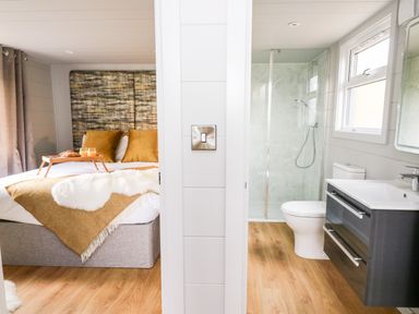 A bedroom with a bed and breakfast tray and an adjoining bathroom with a shower and toilet at Doe Lodge in Nantmel near Rhayader