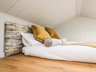 A bed with pillows and a headboard in a room with wooden floor and white paneled walls at Doe Lodge in Nantmel near Rhayader