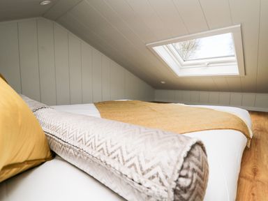 A low bedroom with a bed, pillows, and a skylight window at Doe Lodge in Nantmel near Rhayader