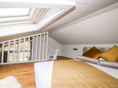 A bedroom loft with a slanted ceiling a bed with pillows a blanket and a skylight window at Doe Lodge in Nantmel near Rhayader