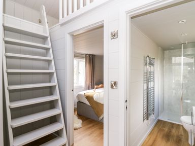 A hallway with a wooden staircase leading up and doors to a bedroom and a bathroom at Doe Lodge in Nantmel near Rhayader