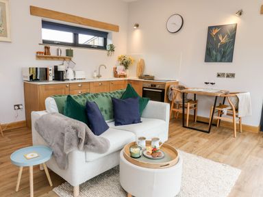 A small open plan kitchen and living area with a white sofa and wooden dining table at Tin Shed in Nantmel near Rhayader