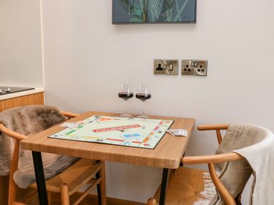 A table with a Monopoly board game two glasses of red wine and two wooden chairs in a room at Tin Shed in Nantmel near Rhayader