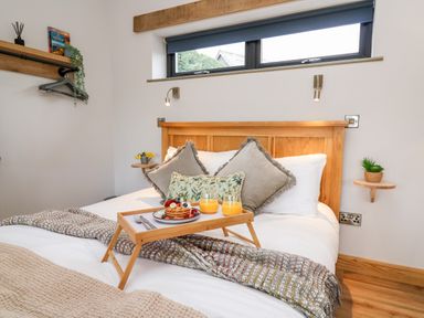 A bedroom with a wooden bed frame and breakfast tray on the bed at Tin Shed Nantmel near Rhayader