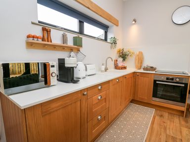 A kitchen with wooden cabinets white countertop microwave coffee maker toaster oven and sink at Tin Shed in Nantmel near Rhayader