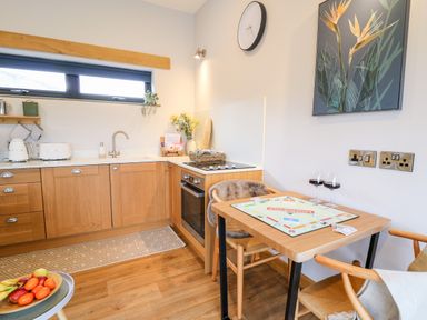 A kitchen with wooden cabinets and a dining table with Monopoly game and two glasses of wine at Tin Shed in Nantmel near Rhayader